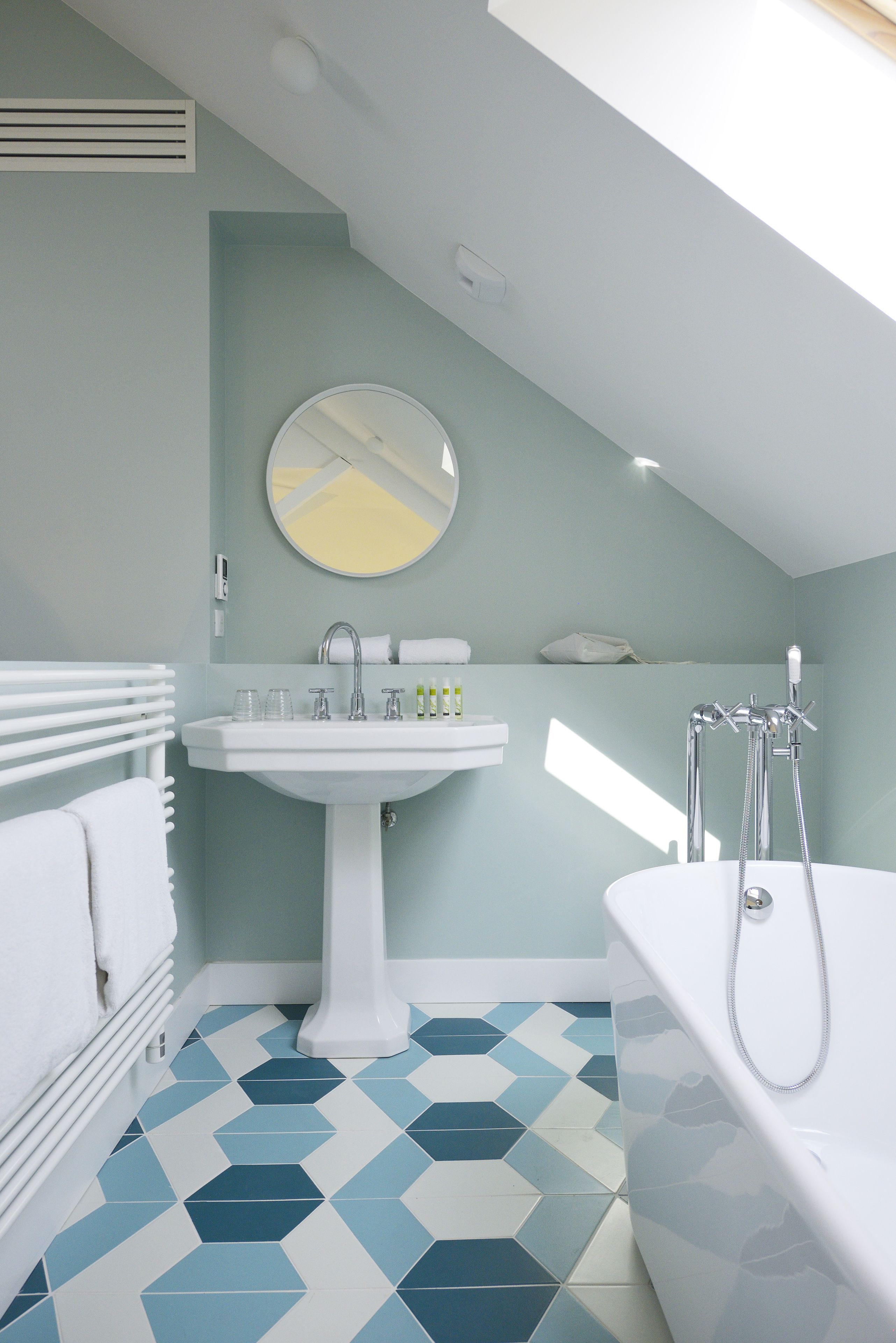 Un baño moderno con un lavamanos blanco, un espejo redondo, una bañera y un toallero blanco.