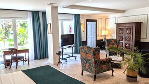 Habitación de hotel con cama, escritorio, televisión, dos sillones, armario y planta en maceta.