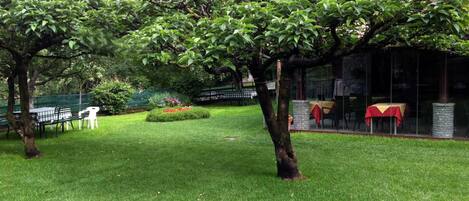 Un jardín bien cuidado con césped, algunos árboles y mobiliario de exterior.