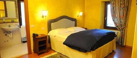A hotel room with a bed, bedside table, lamp, and a view of the bathroom.