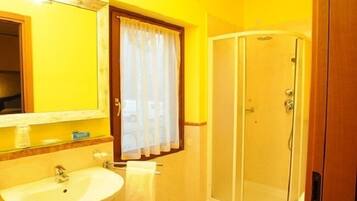 Un baño con lavamanos, espejo, ducha y ventana con cortinas.