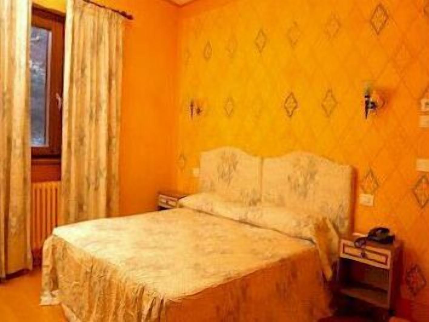 Una habitación con cama, mesita de noche, ventana con cortinas y pared con diseño geométrico.