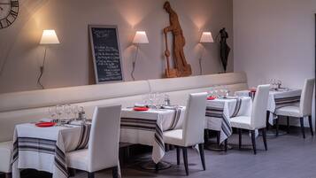 A restaurant with white tables and chairs, a chalkboard menu, and wall-mounted lamps.