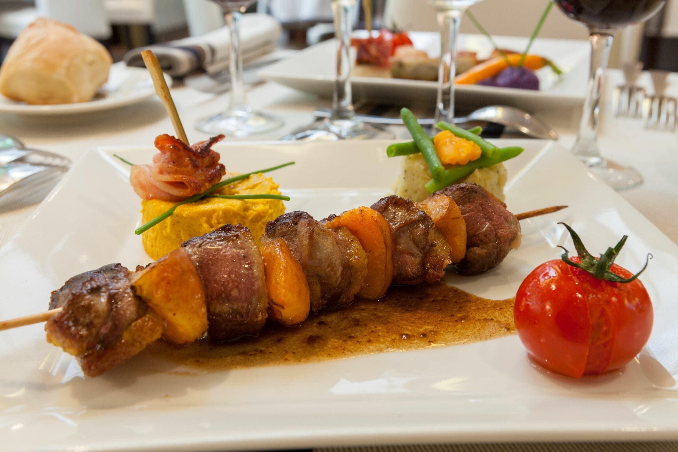 A plate with skewers of meat and vegetables, a tomato, and a small mound of yellow food, possibly scrambled eggs, on a white plate.