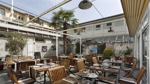 An outdoor dining area with wooden tables and chairs, umbrellas, and a view of the street. - The Originals City, Hôtel Les Thermes de l'Avenue (Dax)