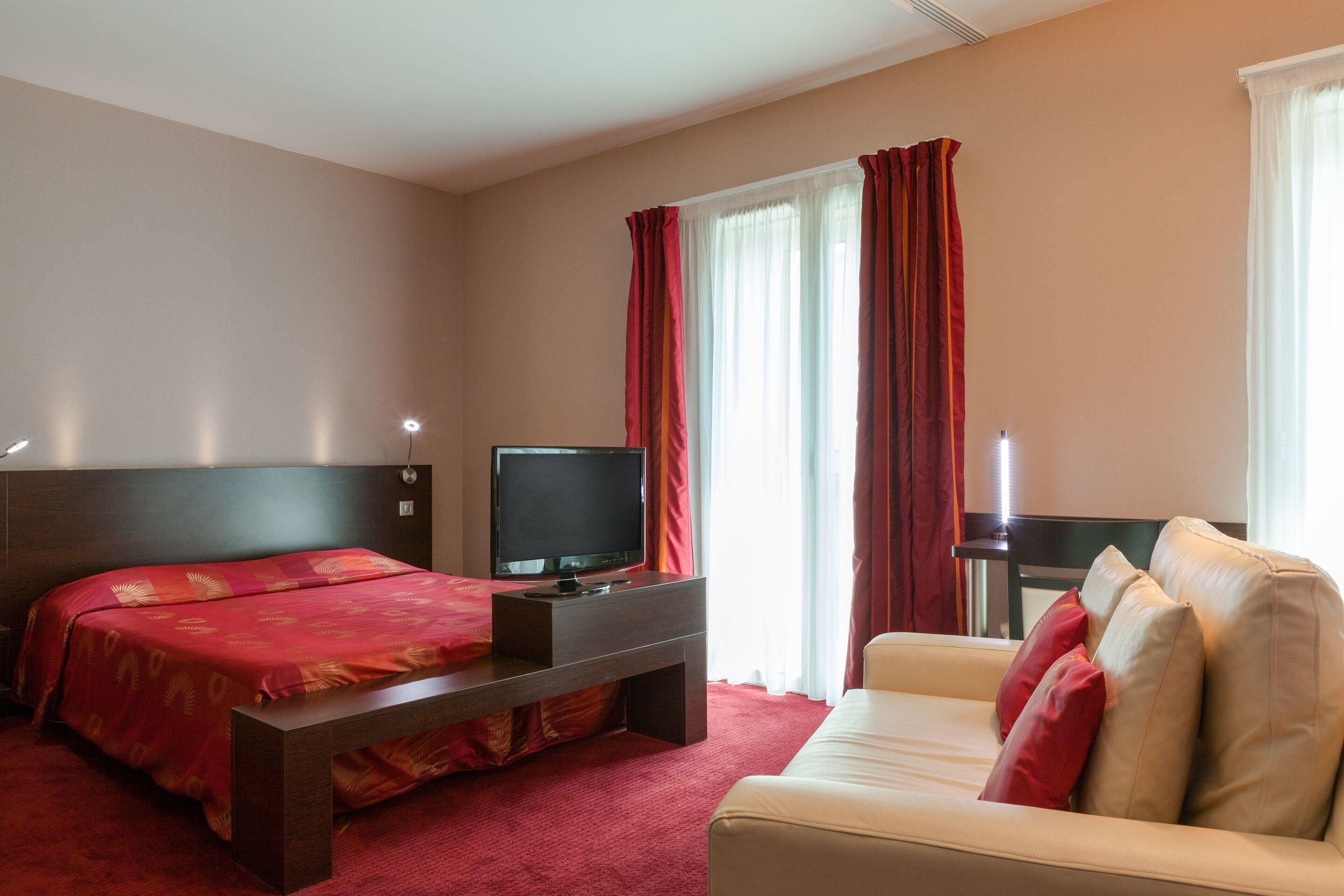 Hotellihuone, jossa on sänky, televisio, sohva ja työpöytä.