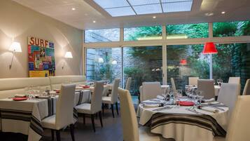 A restaurant with tables set for dining, a 'SURF' poster on the wall, and a view of greenery outside.