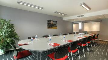A conference room with a long table, red chairs, water bottles, and a projector screen.