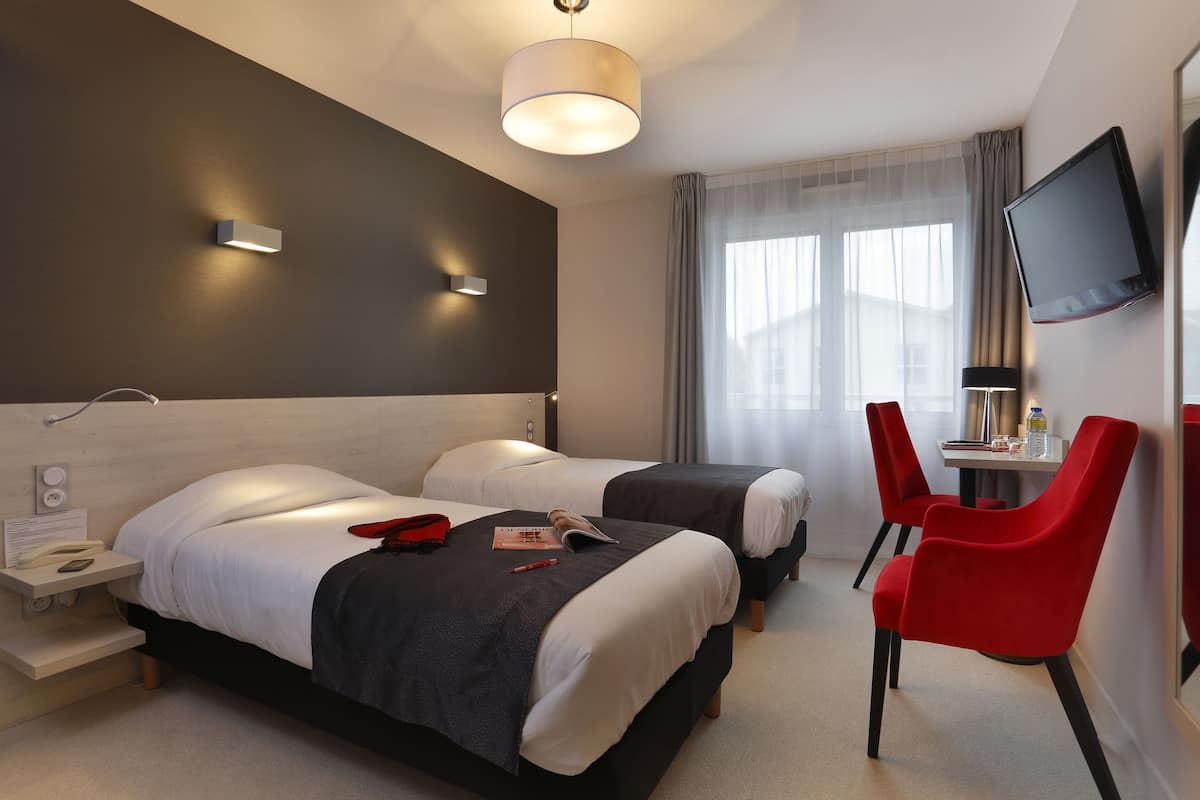 Ein Hotelzimmer mit zwei Betten, einem Schreibtisch mit Stuhl, einem Fernseher und einem Nachttischchen mit Telefon.