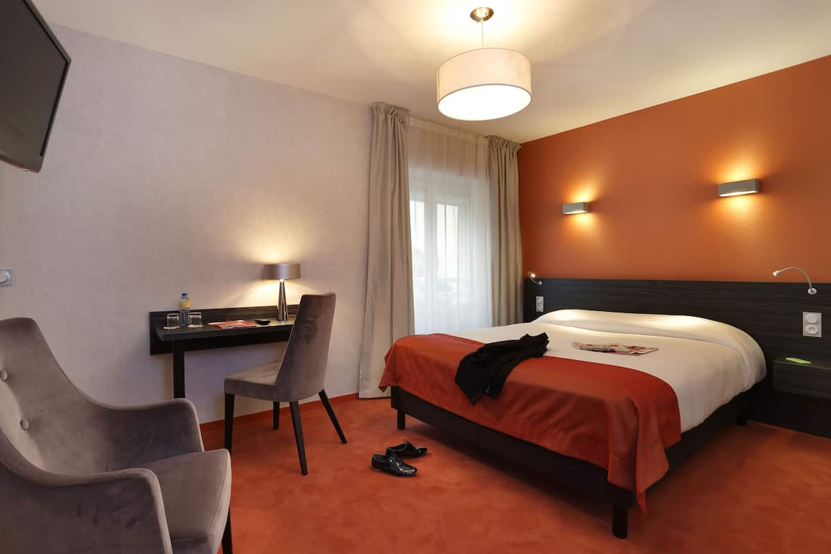 Ein Hotelzimmer mit einem Bett, einem Schreibtisch, einem Sessel und einem Fernseher.
