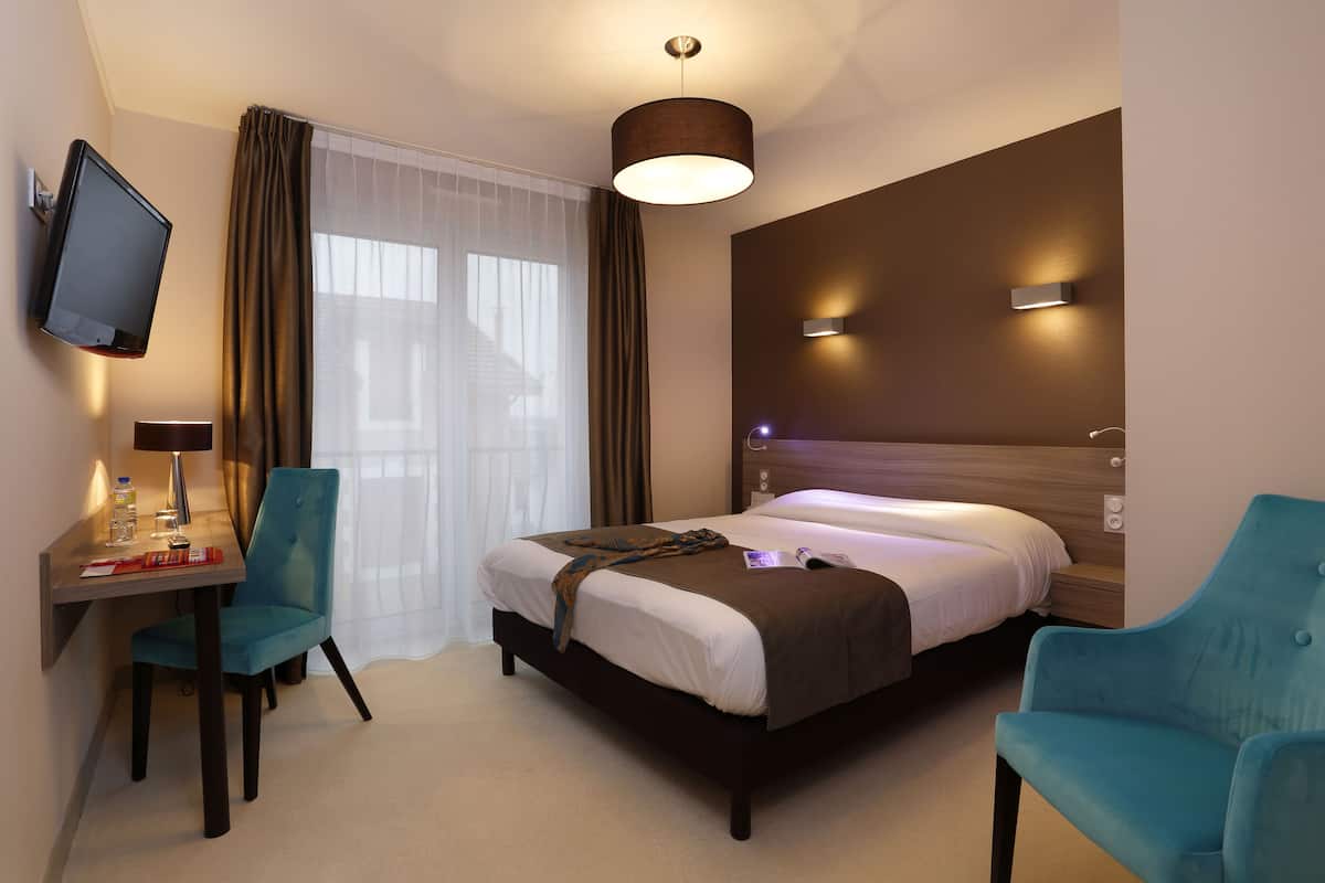 Ein Hotelzimmer mit Bett, Schreibtisch mit Stuhl, Wandfernseher und einem Fenster mit Vorhängen.