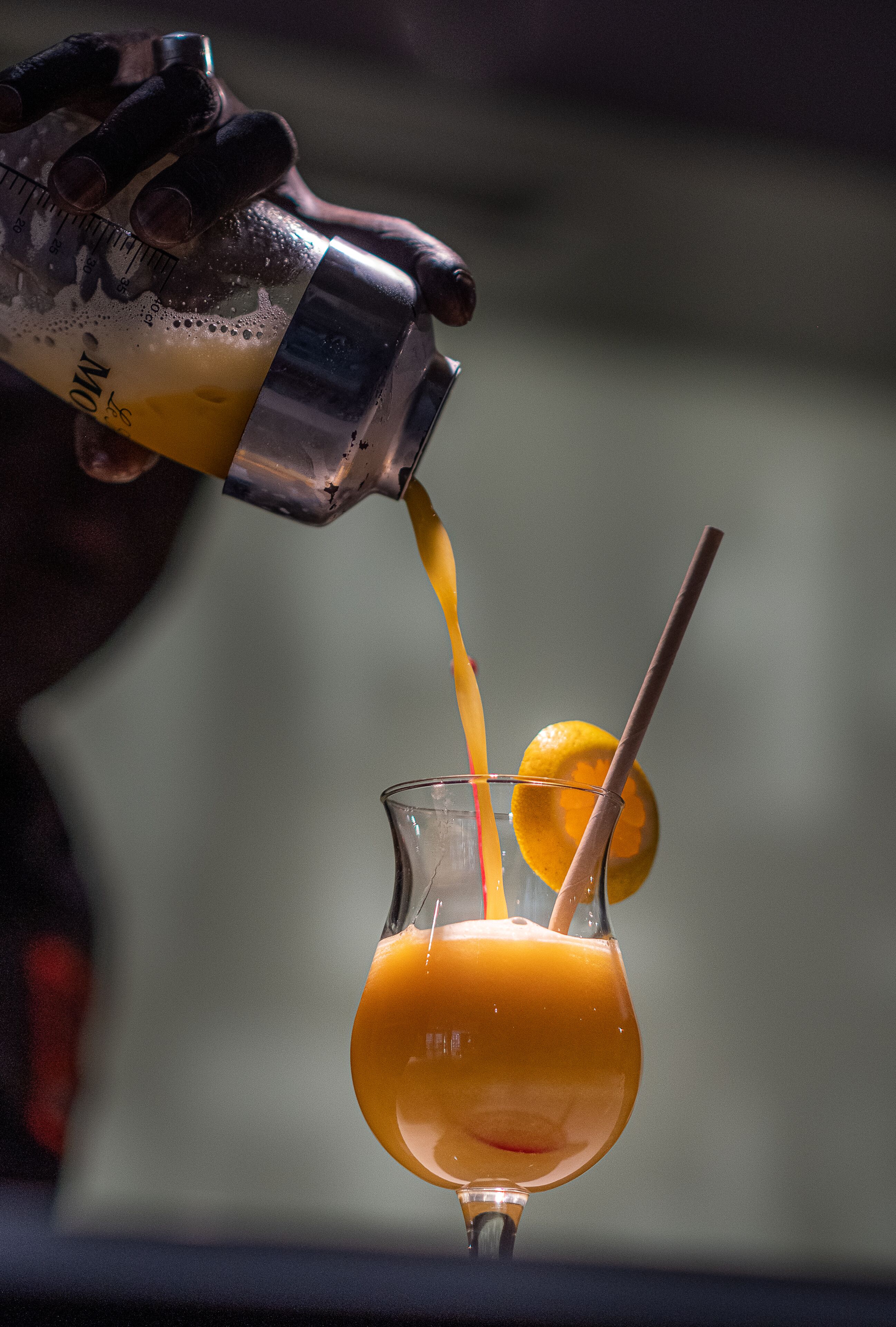 Una mano sirviendo una bebida en un vaso con pajita y una rodaja de limón.
