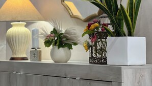 Un mostrador de recepción con un espejo, una lámpara y varios objetos decorativos, como una planta en maceta y flores.