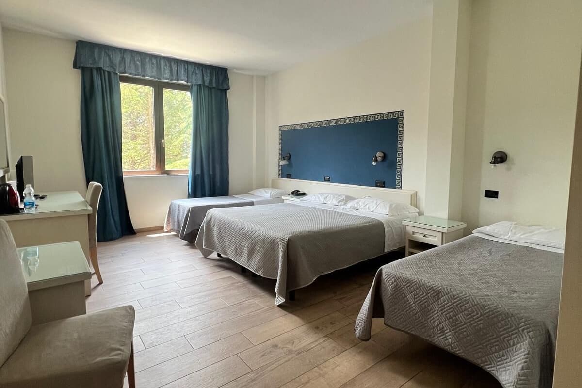 Una habitación de hotel con dos camas individuales, un escritorio, una silla y un ventanal con cortinas.