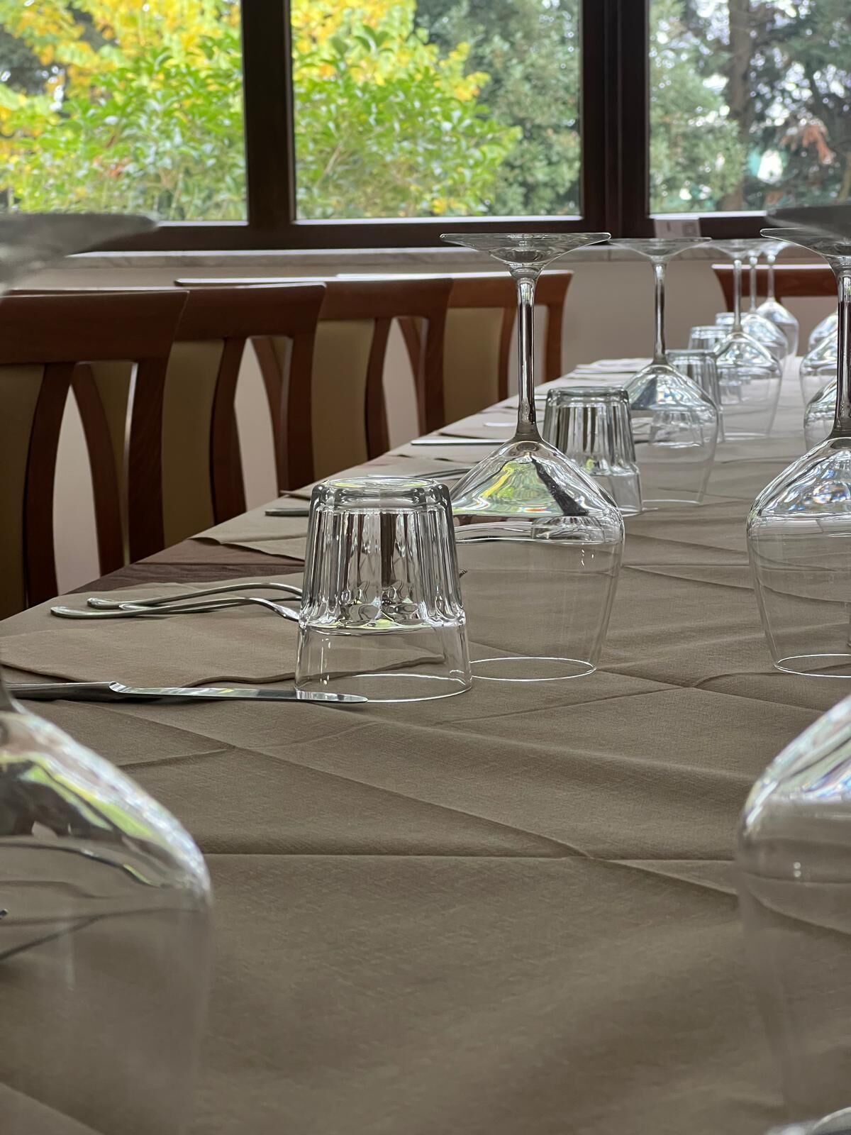 Una mesa de comedor dispuesta con cristalería transparente y cubiertos, con vista a árboles por la ventana.