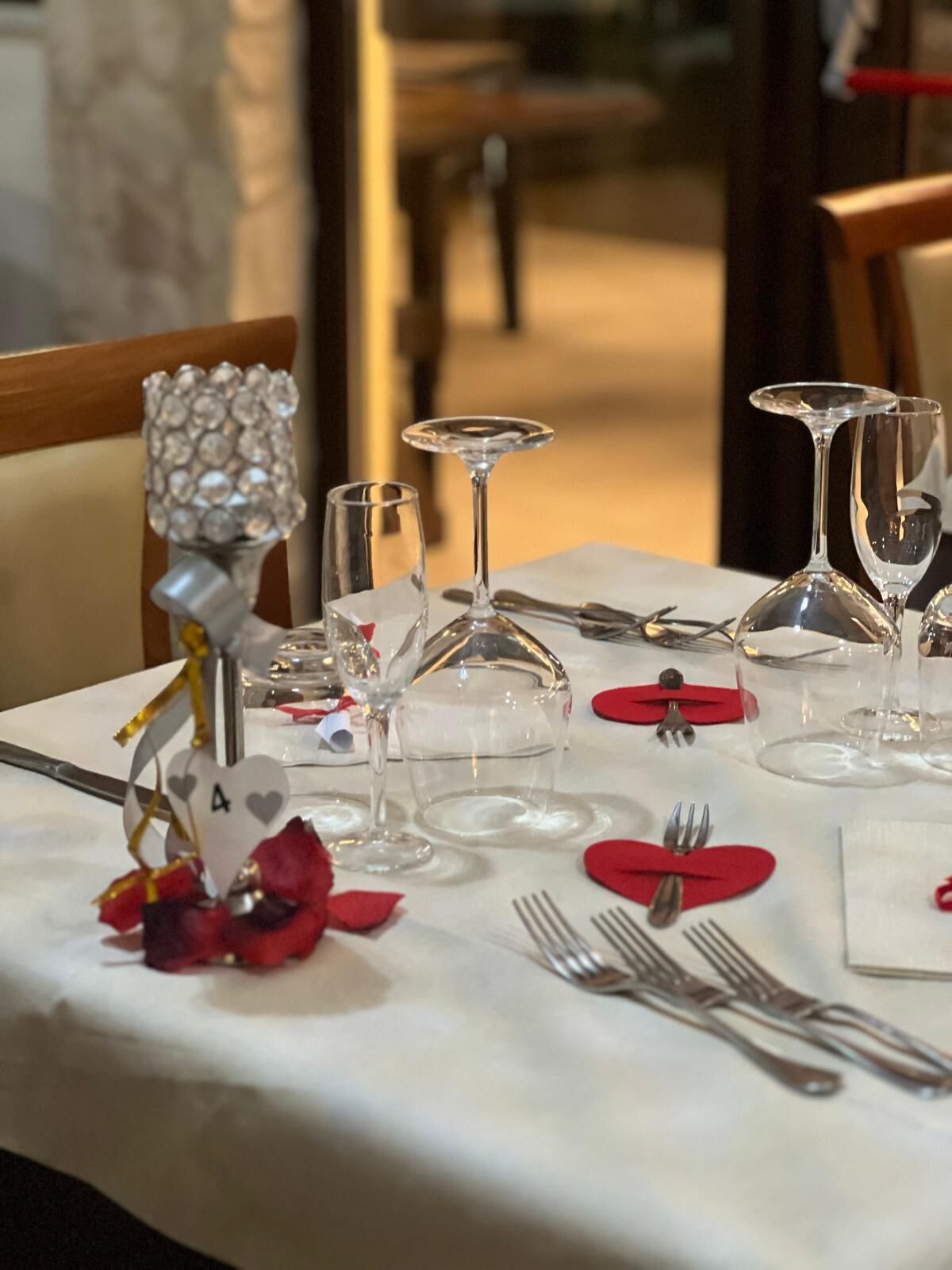 Una mesa de comedor dispuesta con copas de vino, cubiertos y servilletas rojas.