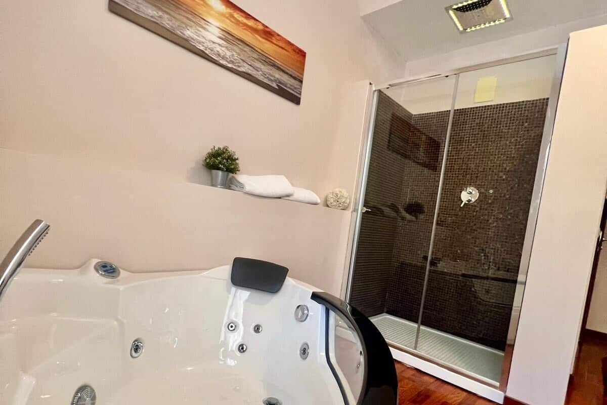 Un baño moderno con una bañera blanca grande, un box de ducha de cristal y un estante pequeño con una planta y una toalla.