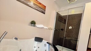 Un baño moderno con una bañera grande, una cabina de ducha de vidrio y un estante pequeño con una planta y una toalla.