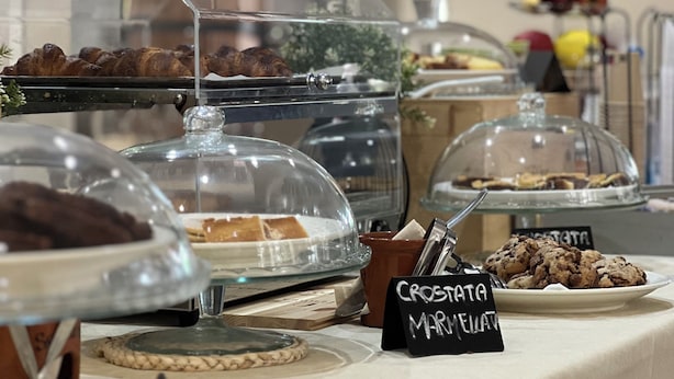 Un bufé con diversas opciones de comida bajo campanas de vidrio, entre ellas, croissants y muffins.