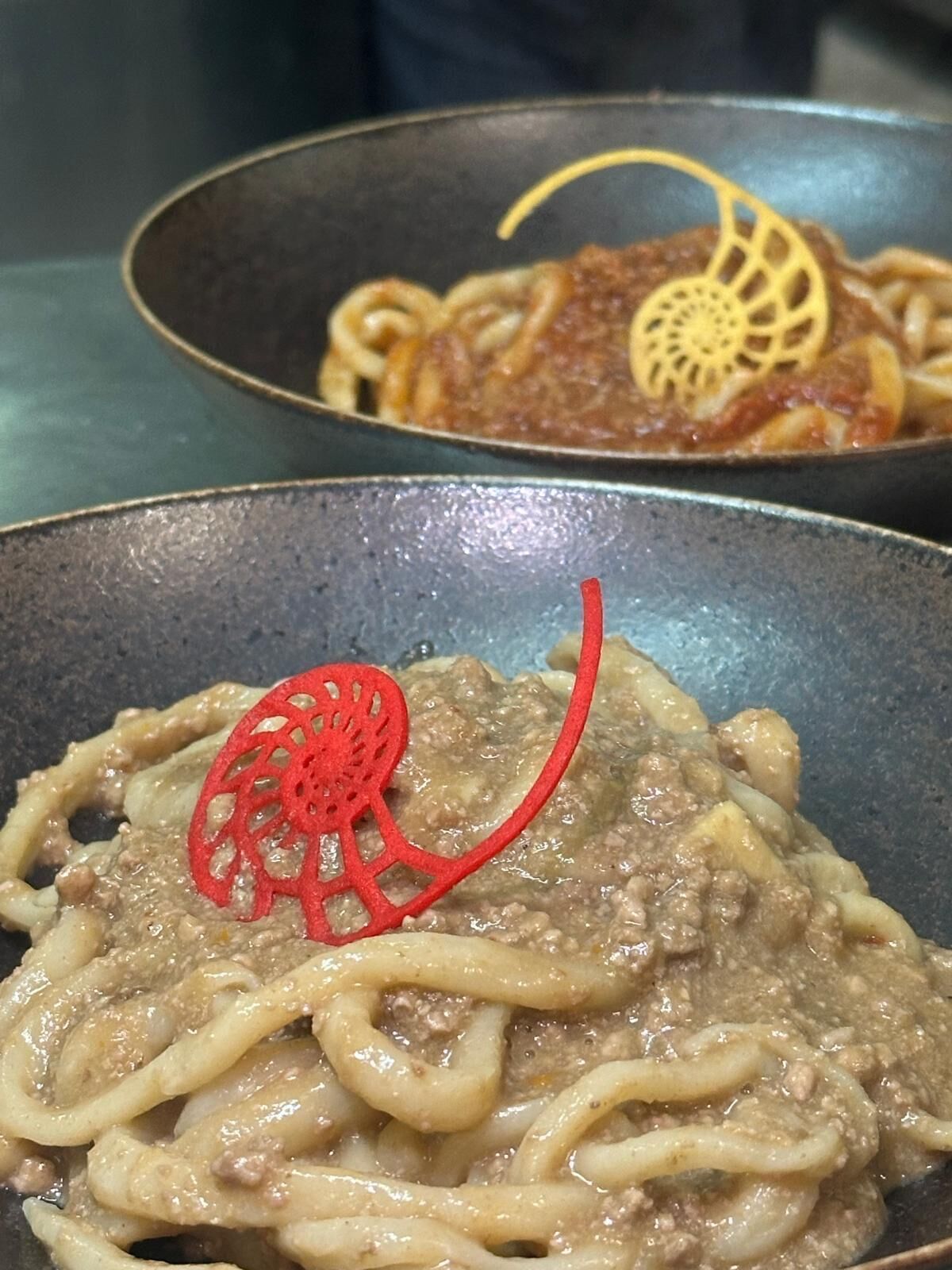 A close-up of a pasta dish with a decorative red element on top.