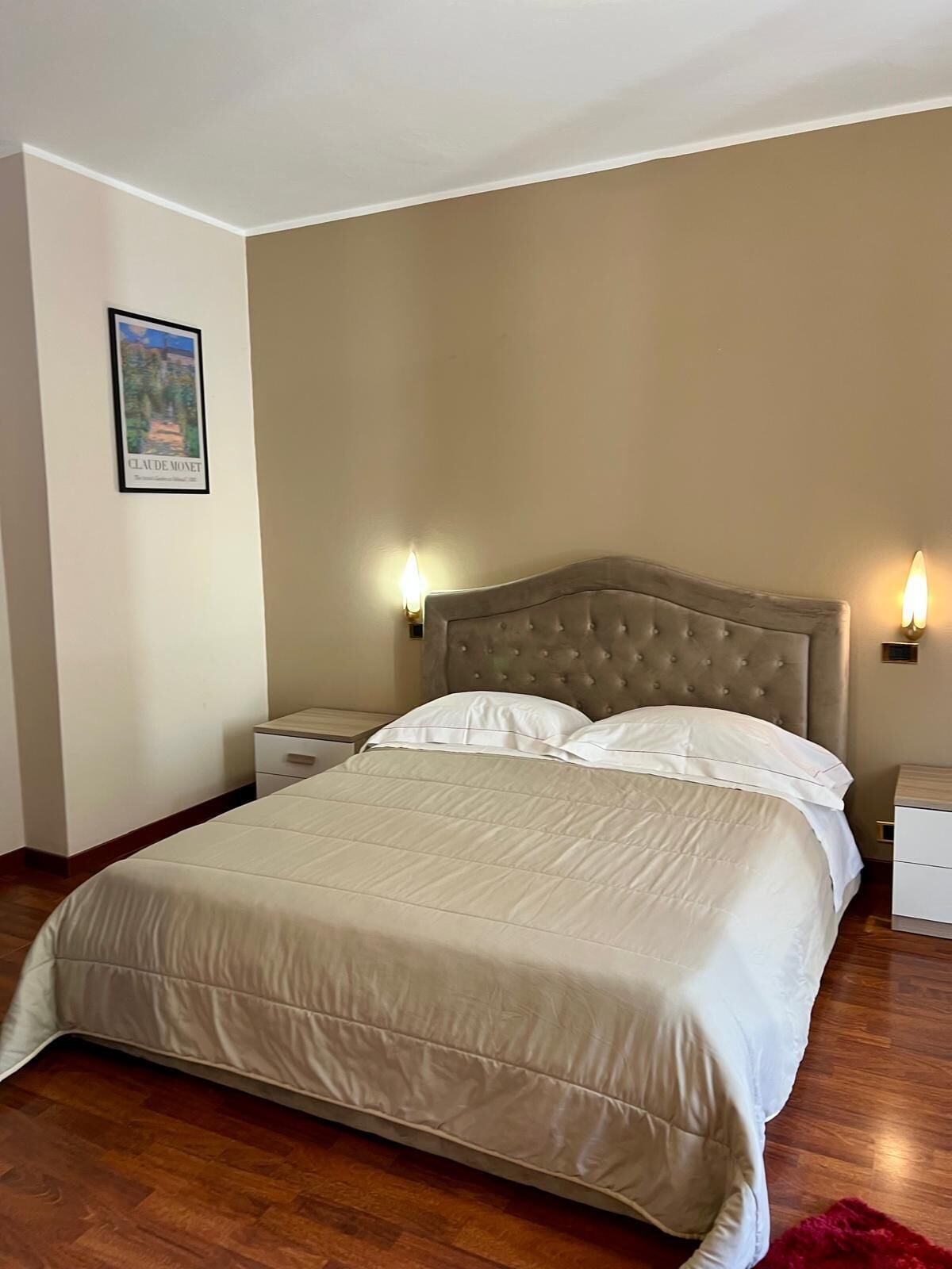 A neatly made bed with a tufted headboard, two bedside tables with lamps, and a framed picture on the wall.