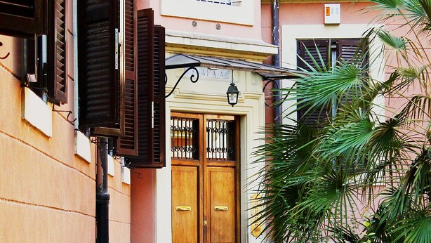 A narrow alleyway with a wooden door at the end, flanked by buildings with shutters and a small garden with palm plants. - Bed & Breakfast A Casa di Lia a Roma (Rome)