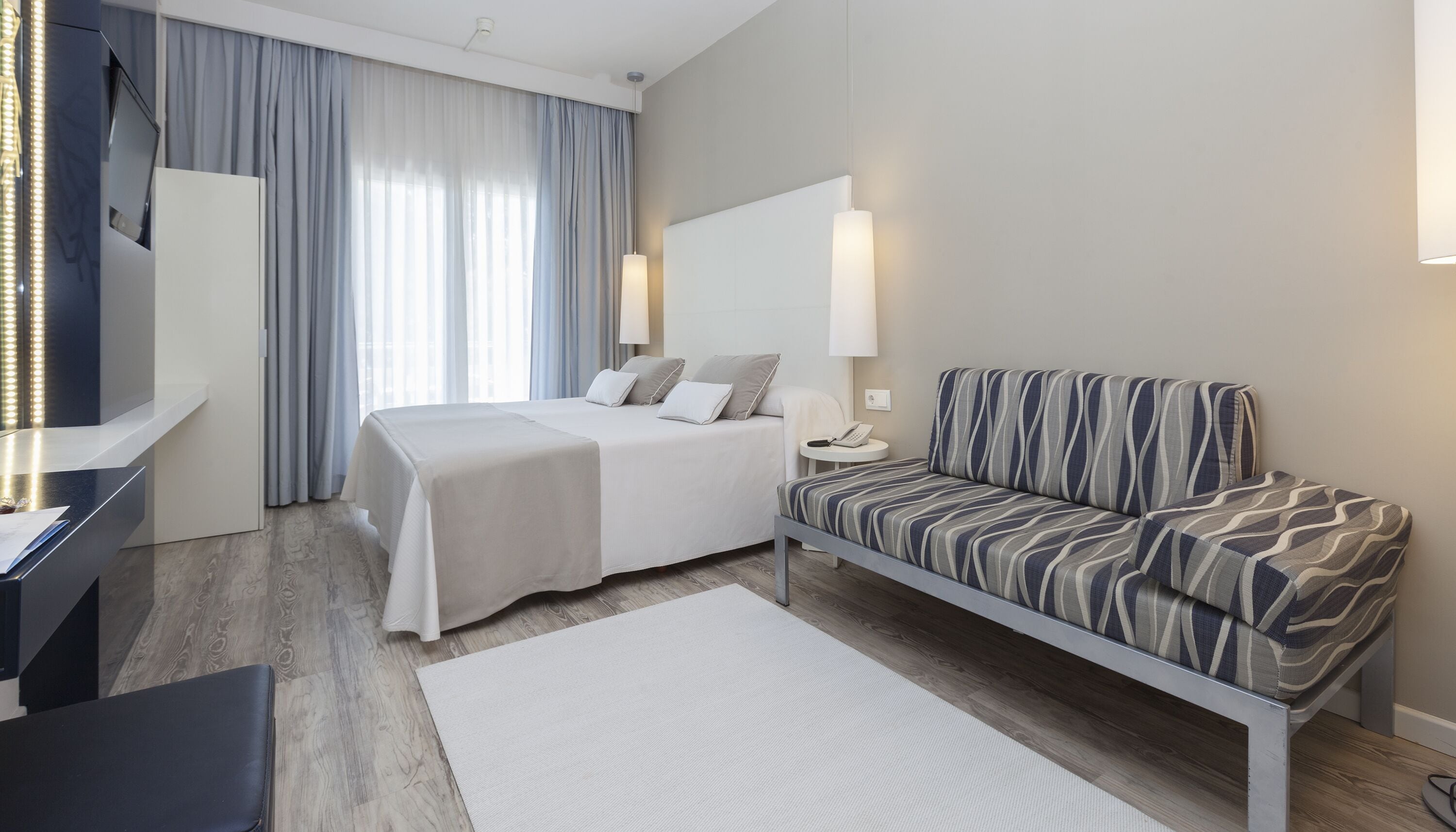 A modern hotel room with a bed, a sofa, a desk, and a large mirror.