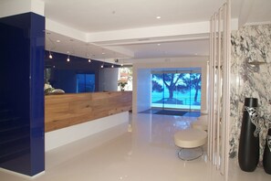 A modern reception area with a wooden counter, a seating area, and a view of trees through large windows. - Canyelles Platja (Roses)