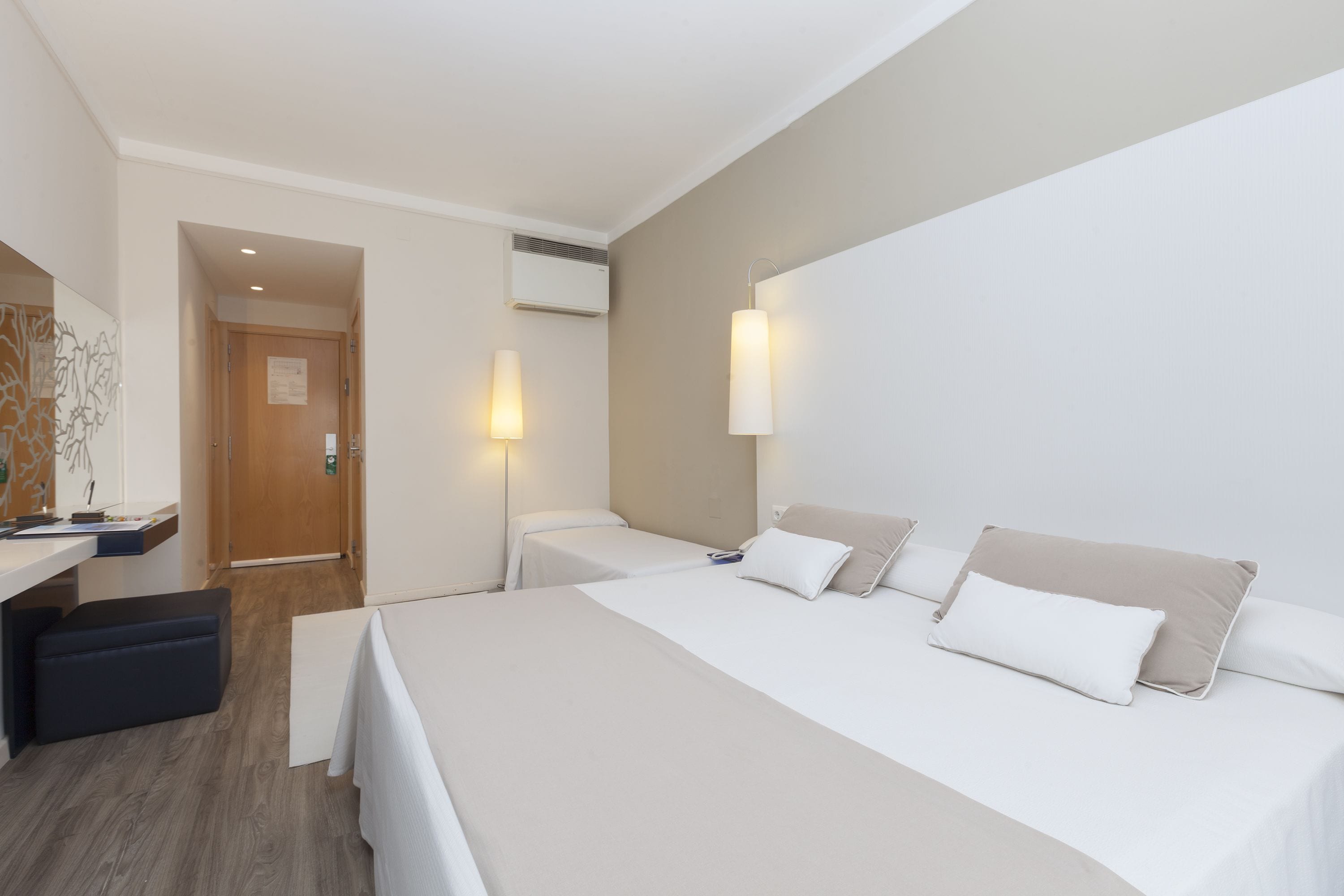 A hotel room with two beds, a desk, and a bench.