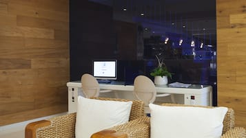 A modern office space with a wooden wall, a desk with a computer, and two wicker chairs with white cushions.