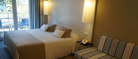 A hotel room with a large bed, a sofa, a bedside table with a phone, and a view of the outdoors through a sliding door.