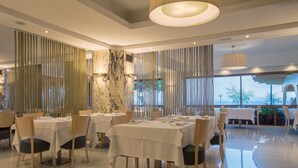 A restaurant with tables set for dining, a marble column, and a view through large windows. - Canyelles Platja (Roses)