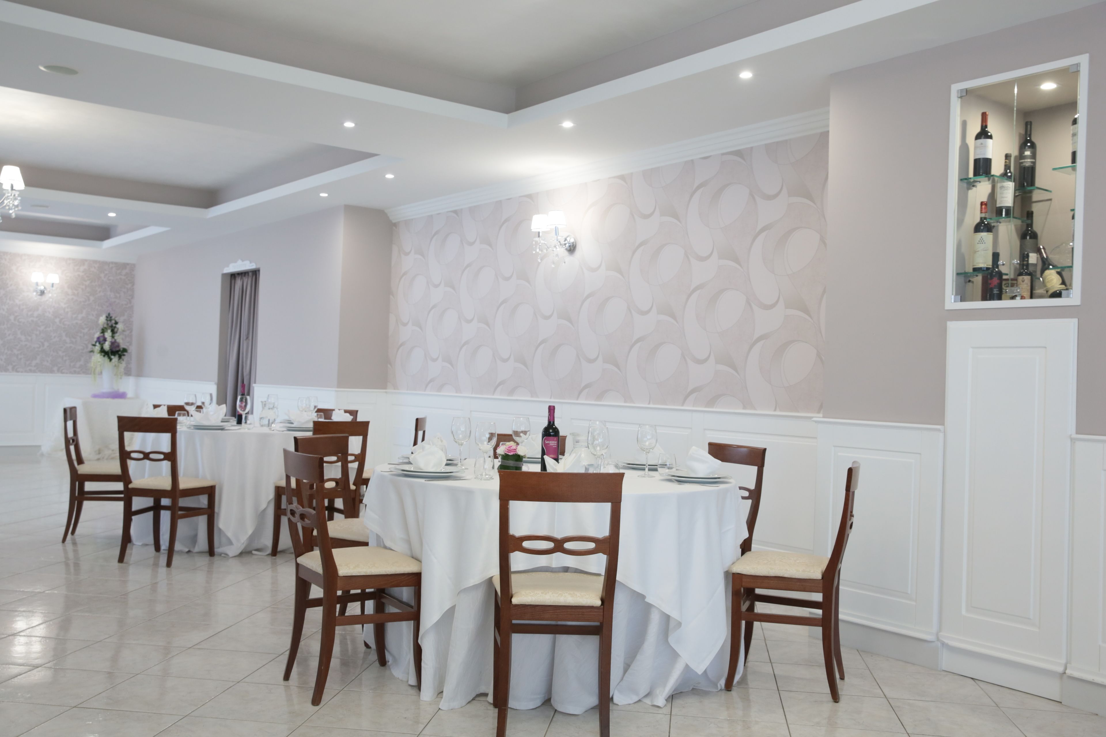 A dining area with round tables, wooden chairs, and a wine display.