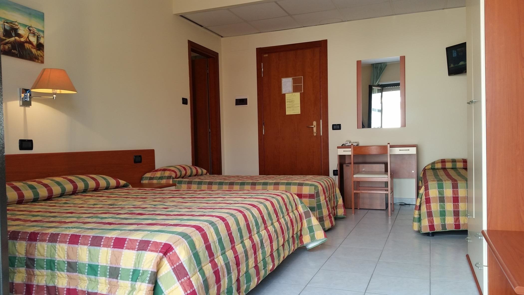 Ein Hotelzimmer mit zwei Betten, einem Schreibtisch, einem Stuhl, einem Spiegel und einer Lampe.
