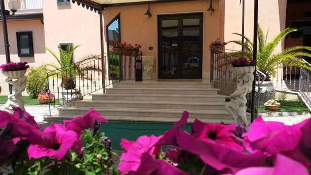 A building entrance with steps leading up to a door, surrounded by potted plants and flowers. - Hotel Leon (San Giovanni Rotondo)