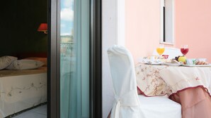 A dining area with a table set for two, a bed with a red lamp, and a view of the city through a glass door. - Hotel Leon (San Giovanni Rotondo)