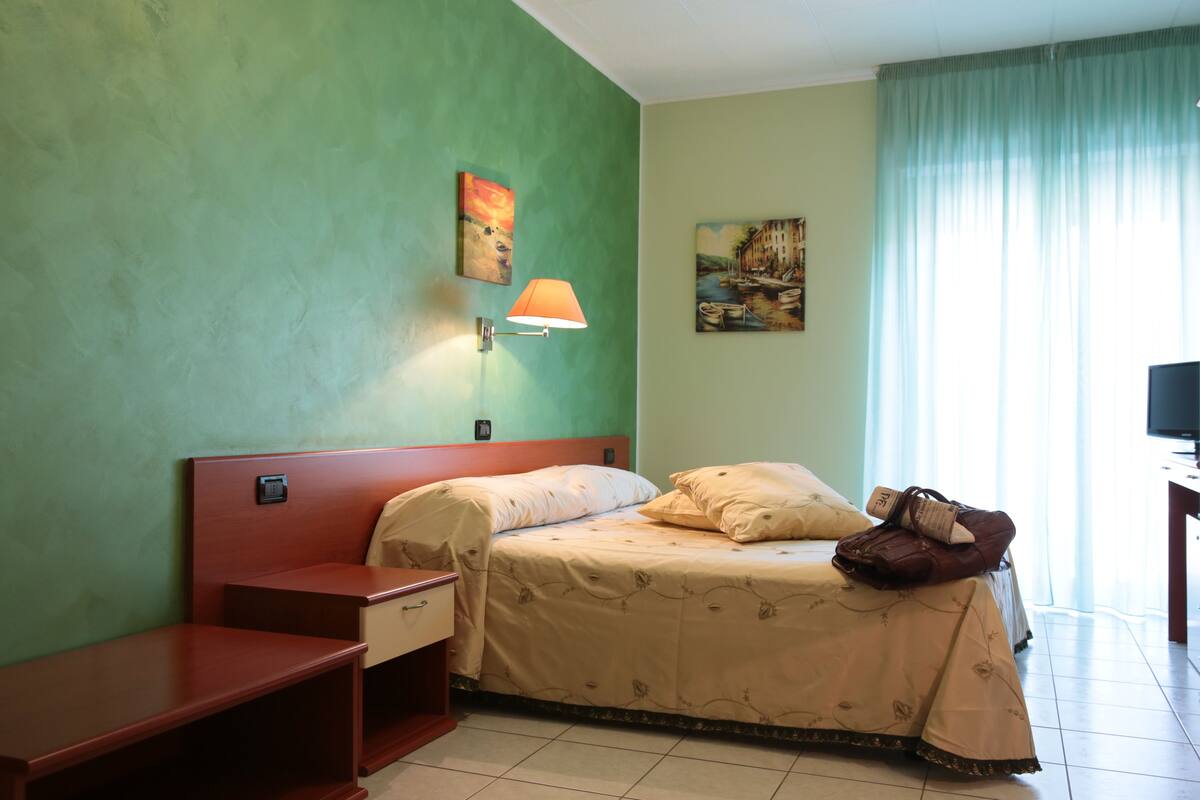 Une chambre d’hôtel avec un lit, une table de chevet, une lampe, une télévision et des œuvres d’art accrochées aux murs.