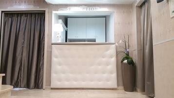 Un área de recepción con una pared capitonada, un mostrador de recepción y una orquídea en maceta.