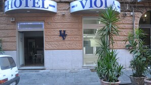 A hotel entrance with a sign reading "HOTEL-VIOLA" and a visible "H" symbol. There are potted plants in front of the entrance. - Hotel Viola (Naples)