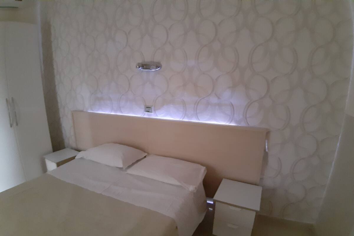 Ein ordentlich eingerichtetes Schlafzimmer mit einem Bett, Nachttischen und einer Wandleuchte.