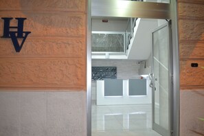 Un moderno vestíbulo de hotel con una recepción, una escalera y vistas del cielo a través de una puerta de cristal.