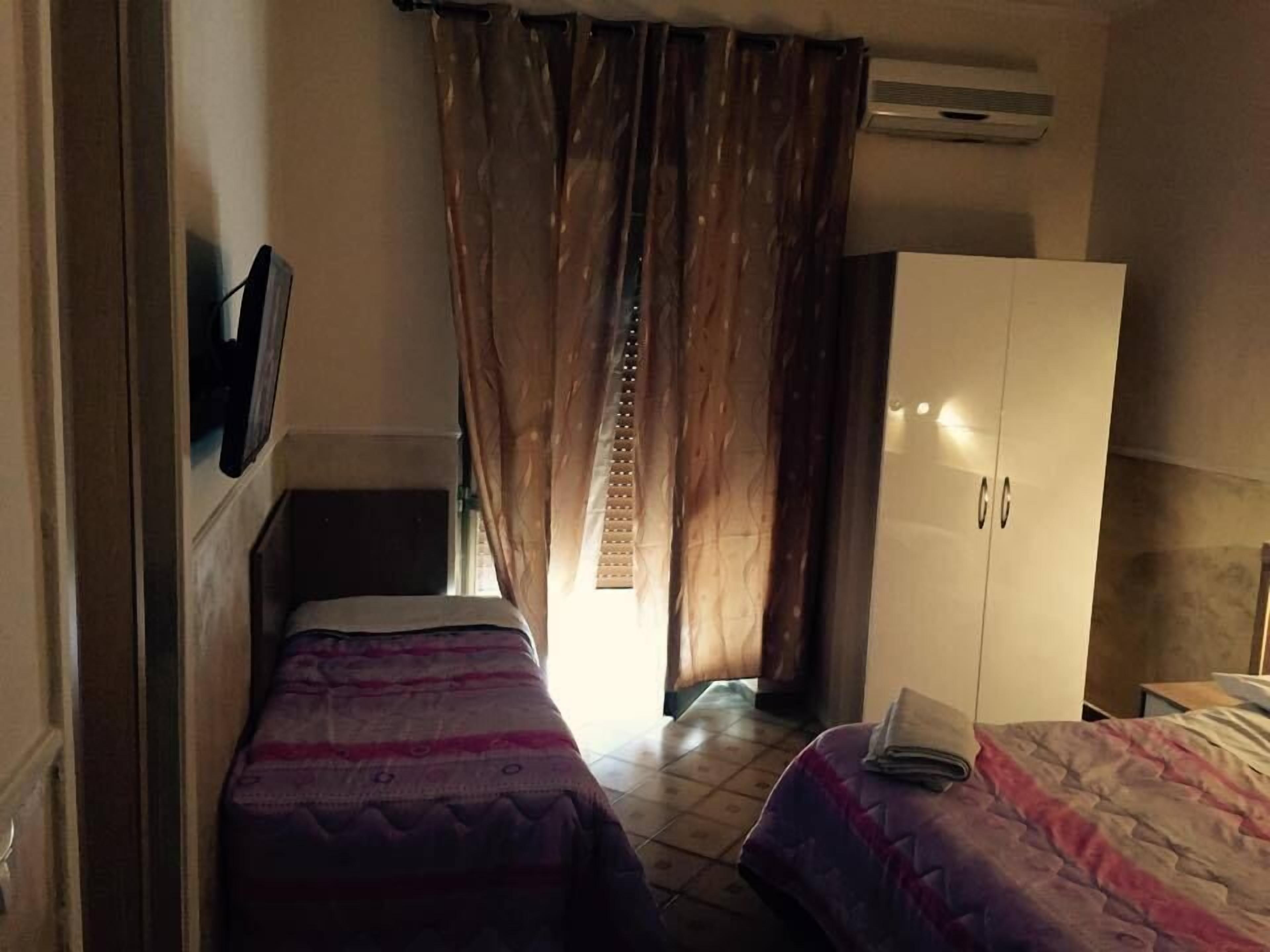A room with two beds, a wardrobe, and an air conditioning unit.