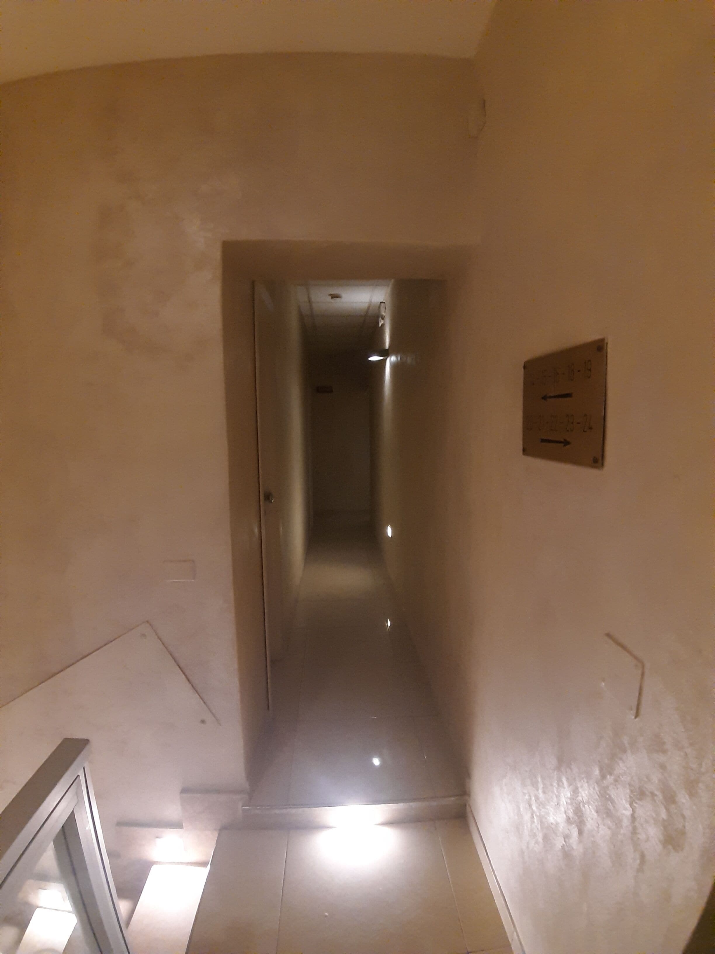 A narrow, dimly lit hallway with a sign indicating room numbers 18-19 and 20-24.