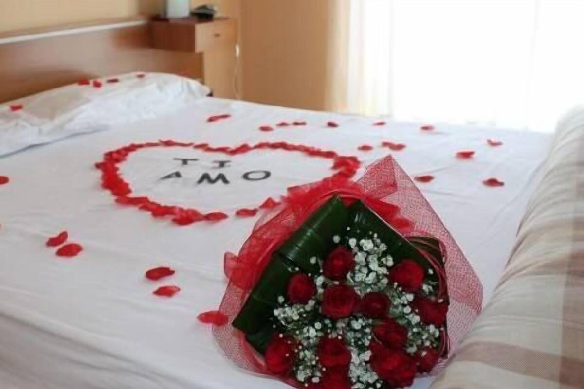 Ein Bett mit einer herzförmigen Anordnung aus Rosenblättern und einem Rosenstrauß.