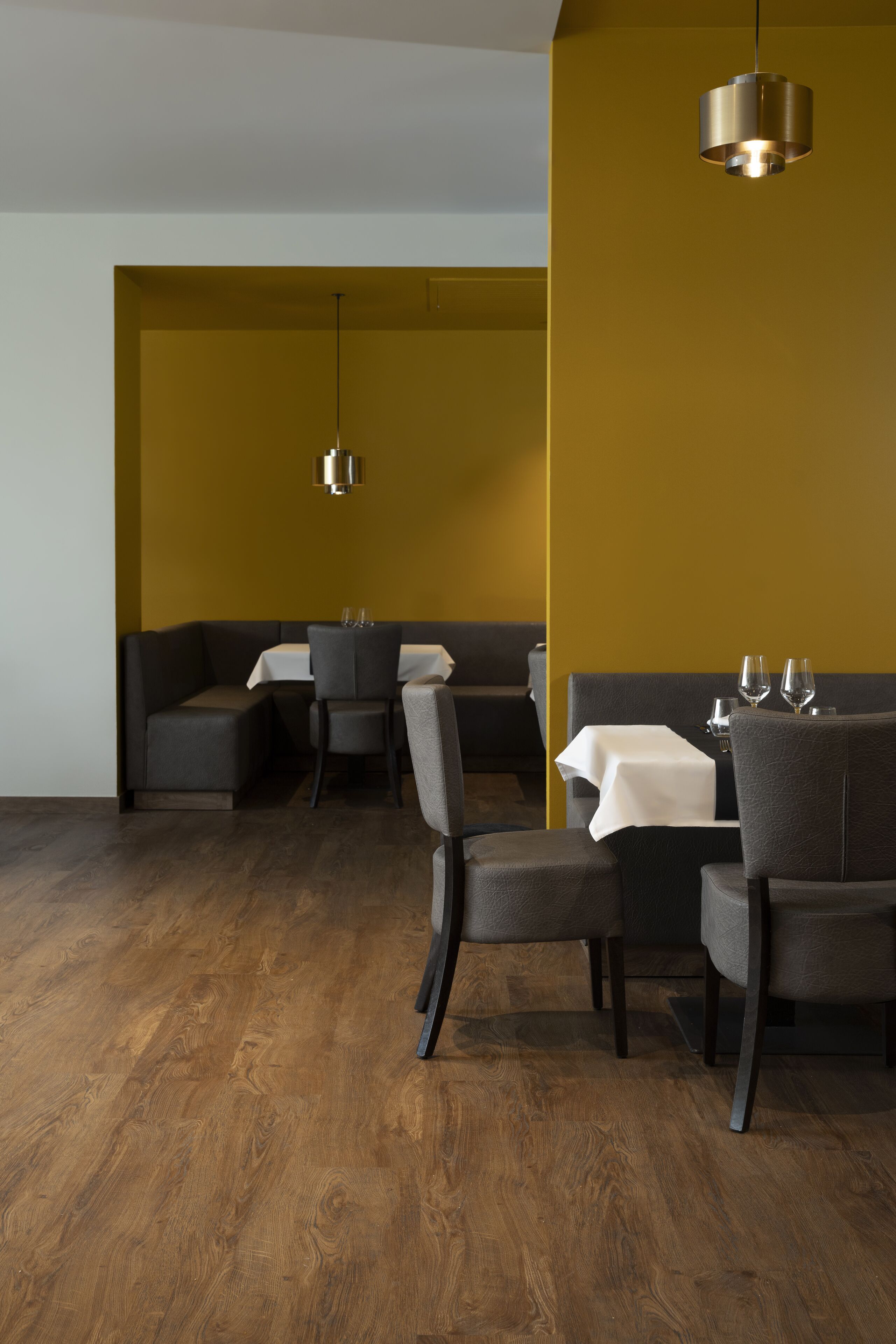 Un comedor moderno con suelo de madera, asientos oscuros y una pared de acento amarilla.