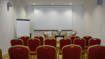 A conference room with rows of red chairs, a whiteboard, and a projector screen.