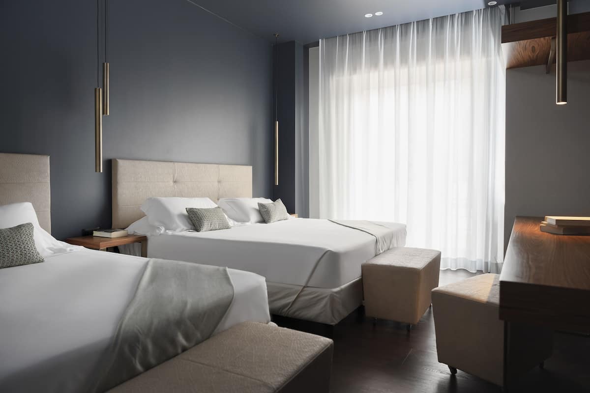 A modern hotel room with two beds, a sitting area, and a large window with curtains.