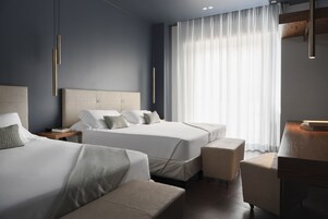 Una habitación de hotel moderna con dos camas, una zona de estar y un gran ventanal con cortinas.