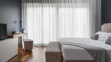 A modern bedroom with a large bed, a bedside table with a lamp, a small stool, and a television on a stand.