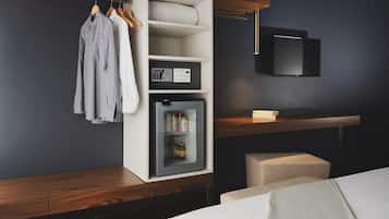 A modern hotel room with a built-in wardrobe, a minibar, a flat-screen TV, and a wooden bench.